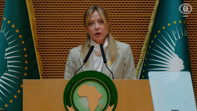 Giorgia Meloni parla al podio dell’Unione Africana ad Addis Abeba, con le bandiere dell’UA sullo sfondo.