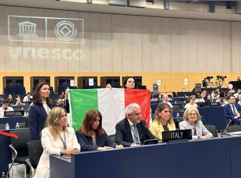 Delegati italiani con bandiera nazionale durante la sessione UNESCO a Busan, con il logo UNESCO proiettato sullo sfondo